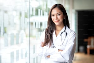 Médecin asiatique souriant en blouse de laboratoire avec les bras croisés contre le regard de la caméra.
