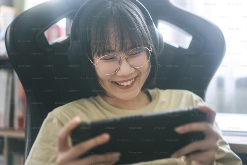 Nerd-Stil junge erwachsene asiatische Gamer-Frau tragen Brille und Kopfhörer spielen ein Online-Spiel. Wettbewerb um Siegesstimmung. Glückliche Menschen Freizeit Lebensstil zu Hause.