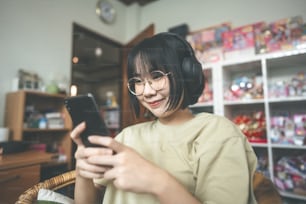 People happy lifestyle satisfation at home concept. Young adult asian woman wear headphone listen music and relax using smartphone for digital social communication.