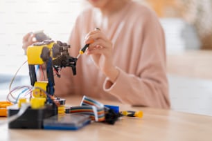 smart asian female programer learning robot arm ai coding electronic board cable in STEM, STEAM she try to testing her autonomous  robotic arm with sensors via Arduino platform at home