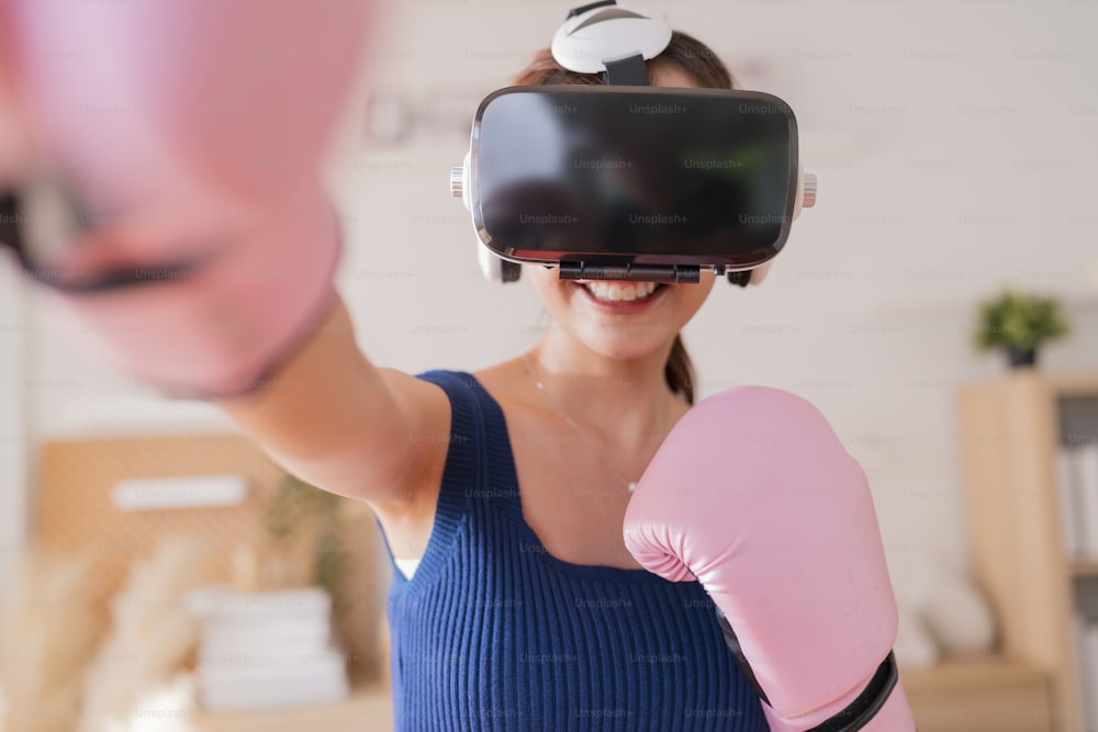 Virtual Metaverse Augmented Reality asian female adult working out boxing in VR headset aerobic training for boxing punch in virtual reality at living room home interior background