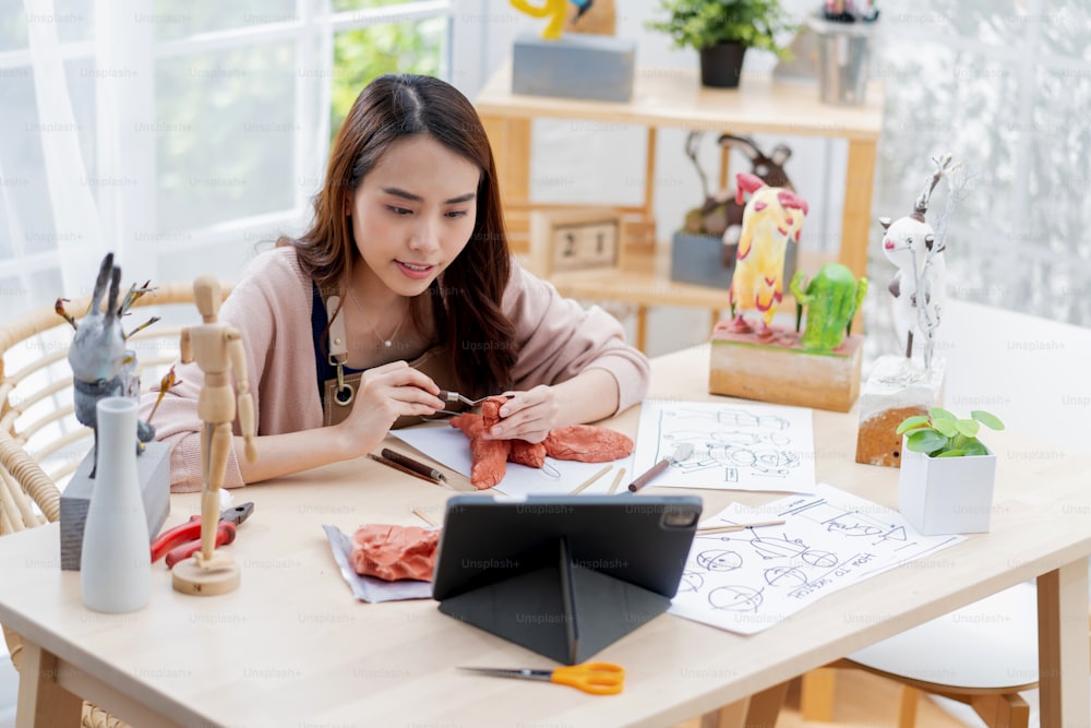 Asian Female spend weekend day for her hobby clay scuplture online course at home, young adult making study from tablet streaming course online in apron costume,asian casual lifestyle at home