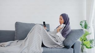 Young Asia muslim lady wear hijab using phone video call talking with doctor consultation or online consultation on sofa in living room at home. Social distancing, quarantine for coronavirus concept.