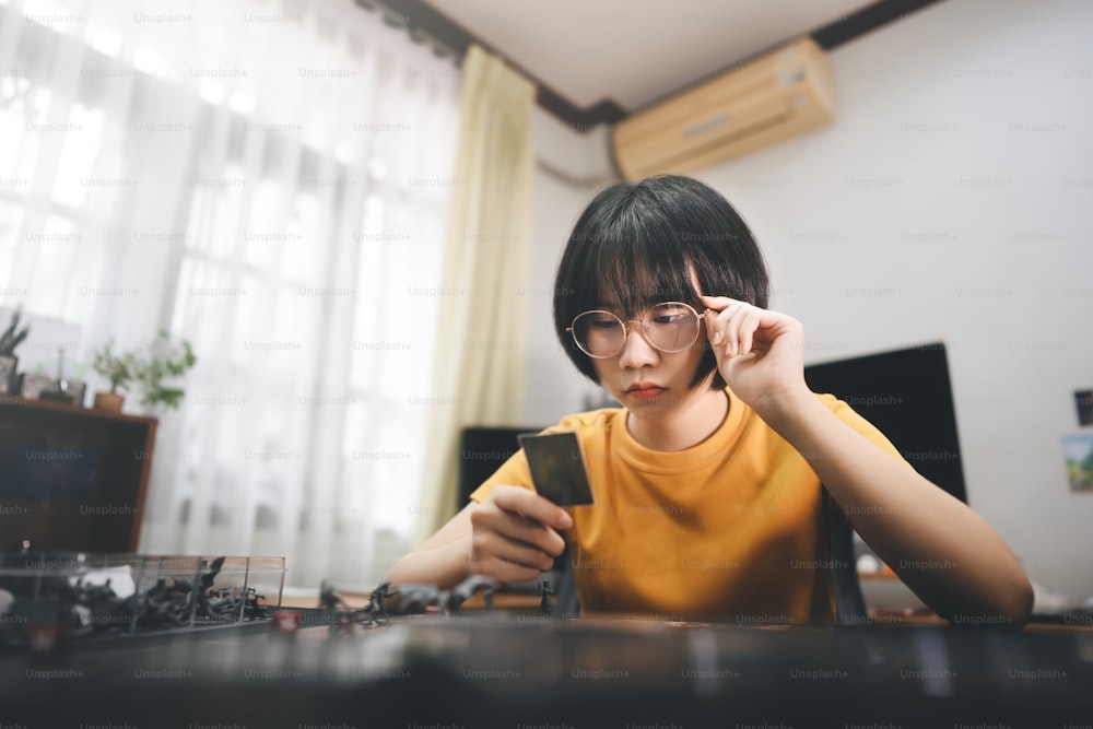 People lifestyle with interesting hobby at home concept. Young adult asian woman solo playing board game on top table. Thinking face and eye looking on card.