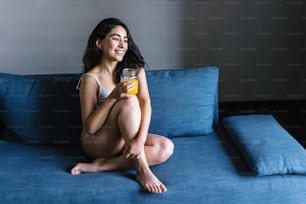 donna latina che beve succo d'arancia mentre riposa sul divano a casa in messico america latina