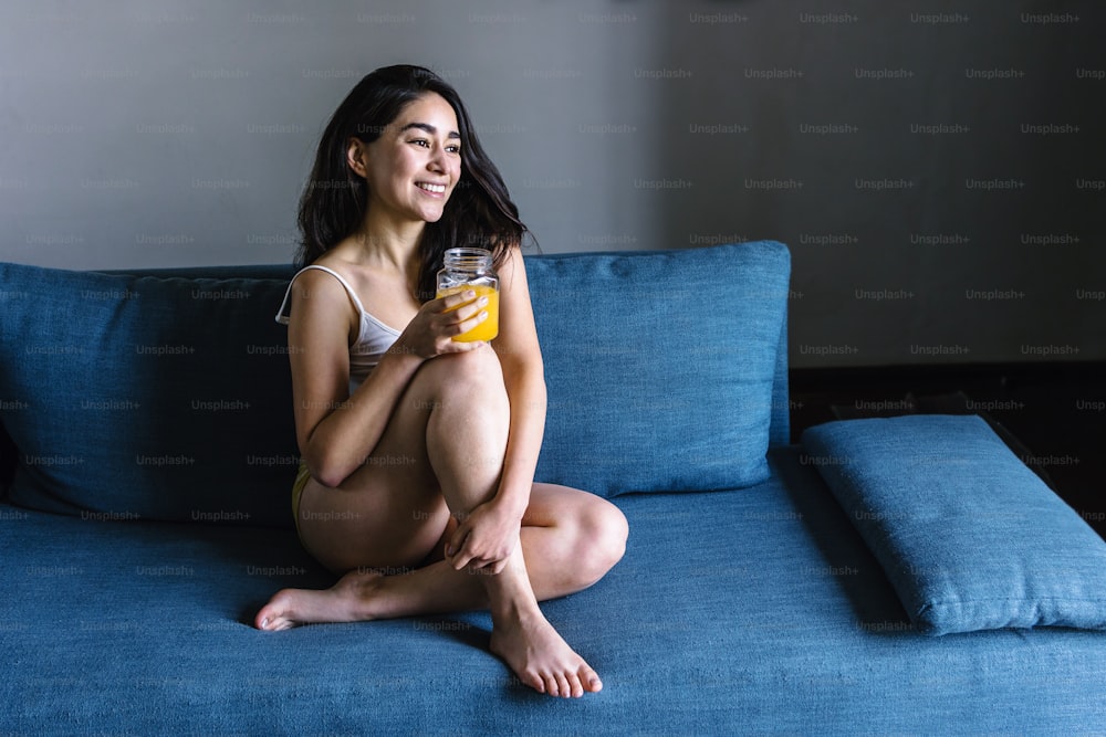 mulher latina que bebe suco de laranja enquanto descansa no sofá em casa no México América Latina