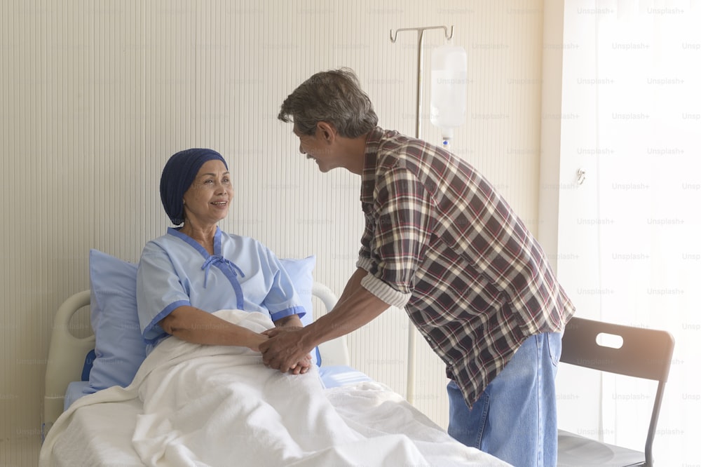Um homem sênior que visita a mulher paciente com câncer usando lenço na cabeça no hospital, cuidados de saúde e conceito médico