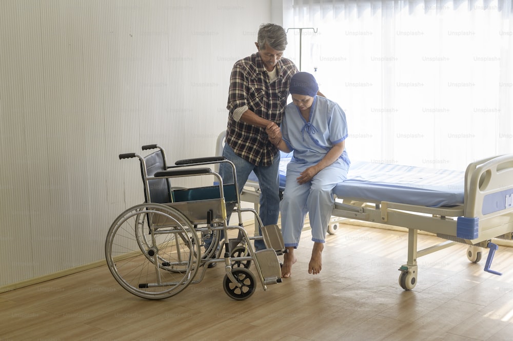 Un homme âgé aidant une patiente atteinte d’un cancer portant un foulard à se déplacer vers des fauteuils roulants à l’hôpital, aux soins de santé et au concept médical