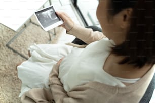 Mujer embarazada asiática mirando la imagen de ultrasonido en casa