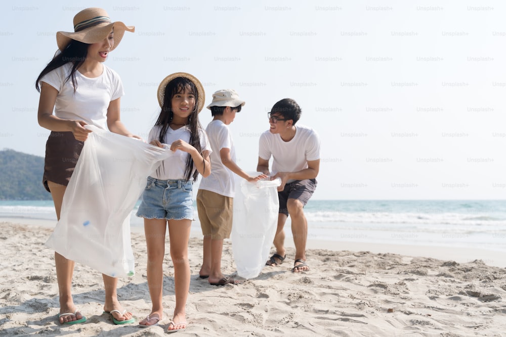Voluntario de una familia asiática recogiendo una botella de plástico en una playa con mar para proteger el medio ambiente