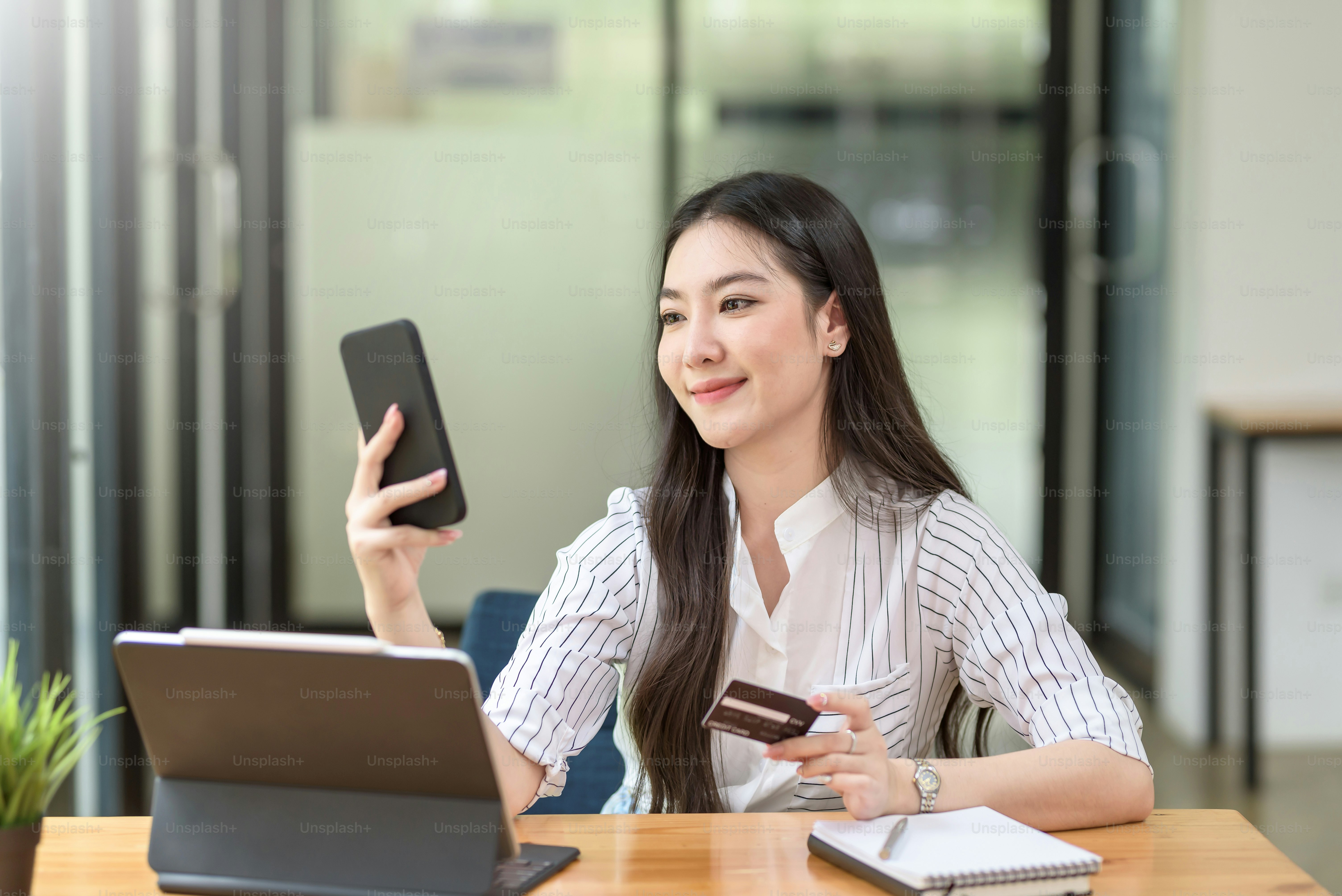 Beautiful young Asian woman holding smartphone and using credit card for online shopping.