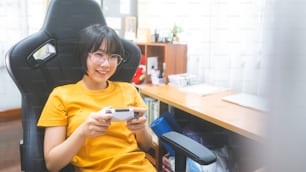 Nerd style young adult asian gamer woman wear eyeglasses play a online game wear yellow shirt. Competition for victory mood. Happy people leisure lifestyle at home.