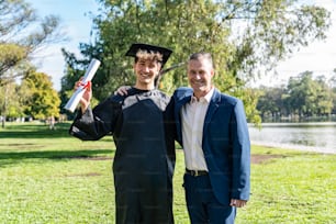 Portrait d’un jeune homme caucasien heureux diplômé avec son père le jour de sa remise des diplômes.  Ils regardent tous les deux la caméra