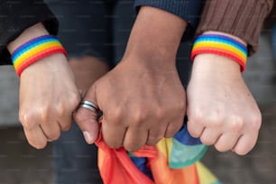 Close up of three hands with   LGBTQ rainbow wristband and holding a Rainbow flag, concept of gay pride month, lesbian pride, LGBT awareness movement, non-binary inclusivity, and diversity