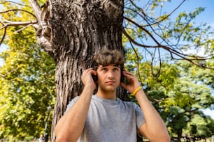 Handsome young man leaning on a tree while listening to music