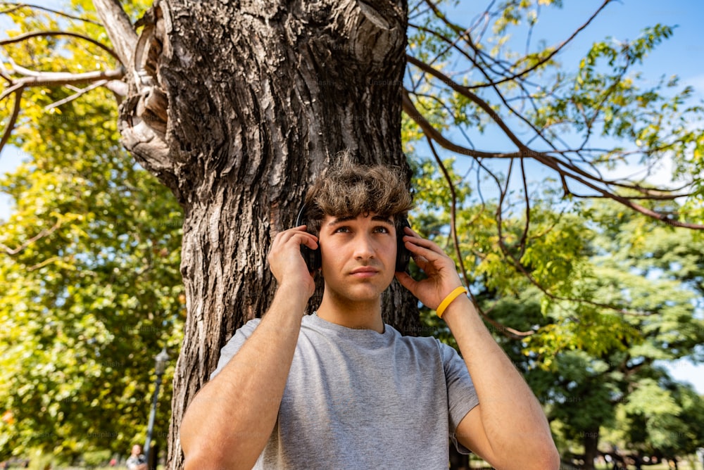Hübscher junger Mann, der sich an einen Baum lehnt und Musik hört