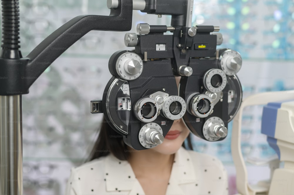 Uma jovem cliente do sexo feminino sendo examinada teste visual usando o dispositivo de medição da visão de optometria bifocal por oftalmologista no centro óptico, conceito de cuidados com os olhos.