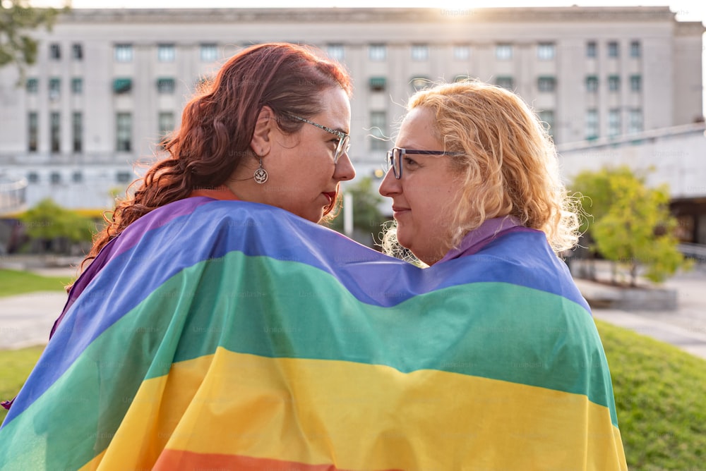 Coppia lesbica sotto la bandiera arcobaleno LGBT mentre si guardano l'un l'altro. Concetto di orgoglio. Mese dell'orgoglio.