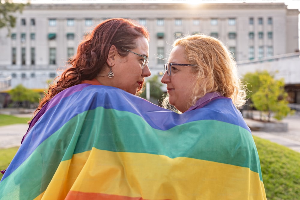 Lesbian couple under LGBT rainbow flag while looking at each other. Concept of Pride. Pride month.