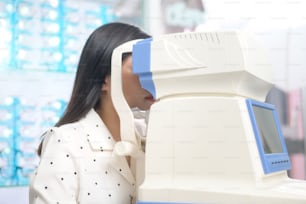 Uma jovem cliente do sexo feminino sendo examinada teste visual usando auto-refrator por oftalmologista em centro óptico, conceito de cuidados com os olhos.
