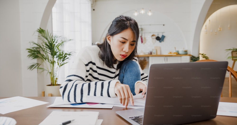 젊은 아시아 여성 프리랜서는 집에서 부엌에서 회사와의 원격 회의를 위한 계정 및 재무 프로젝트를 위해 노트북으로 프레젠테이션 작업에 중점을 둡니다. 여학생은 집에서 온라인으로 학습합니다.
