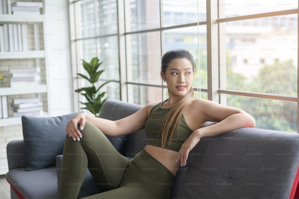 A fit beautiful asain woman in sportswear sitting and relaxing on sofa after workout, health and exercise concept
