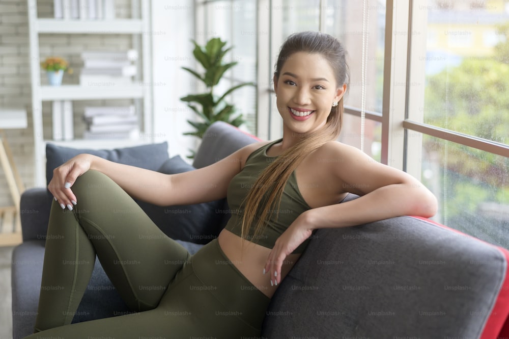 A fit beautiful asain woman in sportswear sitting and relaxing on sofa after workout, health and exercise concept