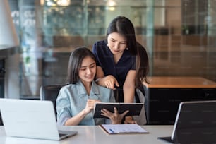 Duas jovens empresárias asiáticas estão felizes trabalhando em apresentações usando papéis e tablet colocados no escritório.