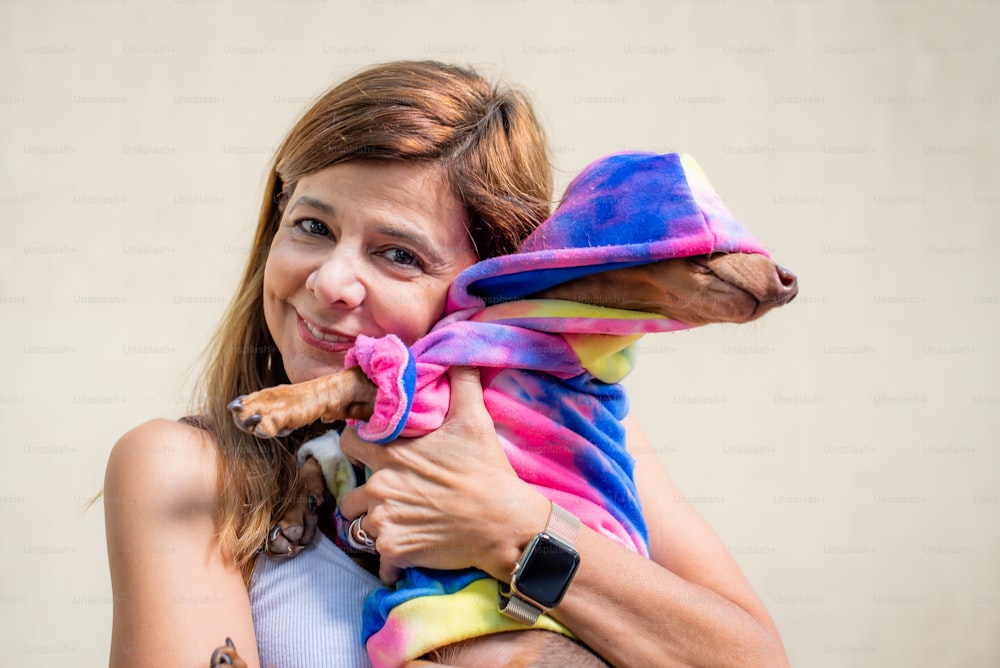 Mujer latina sosteniendo a su perro, ambos vestidos igual. Está mirando a la cámara.
