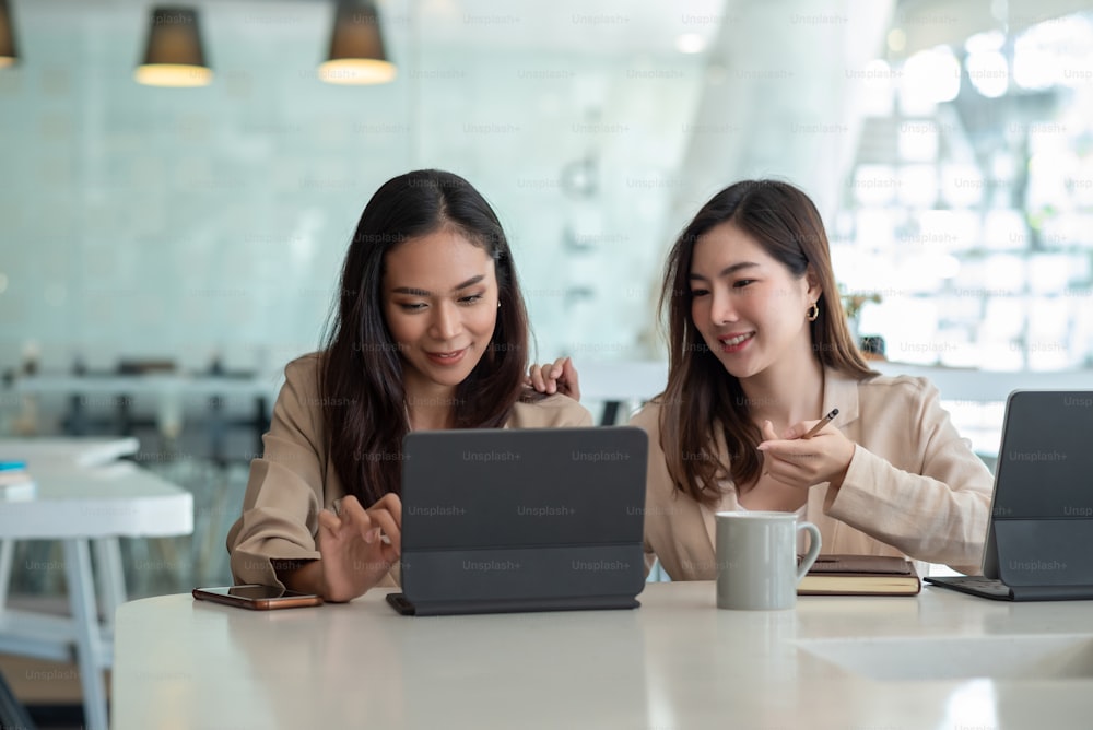 Due giovani imprenditrici asiatiche sono felici di lavorare alle presentazioni utilizzando carte e tablet posizionati in ufficio.