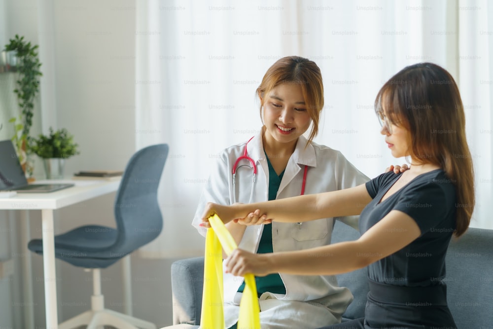Fisioterapeuta mulher asiática supervisiona os pacientes que se esticam com fita elástica.