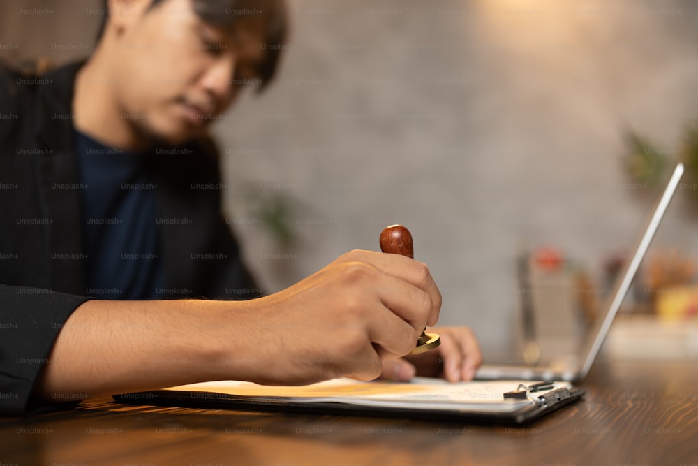 Close-up of a person's hand stamping with approved stamp on certificate document public paper at desk, notary or business people work from home, isolated for coronavirus COVID-19 protection