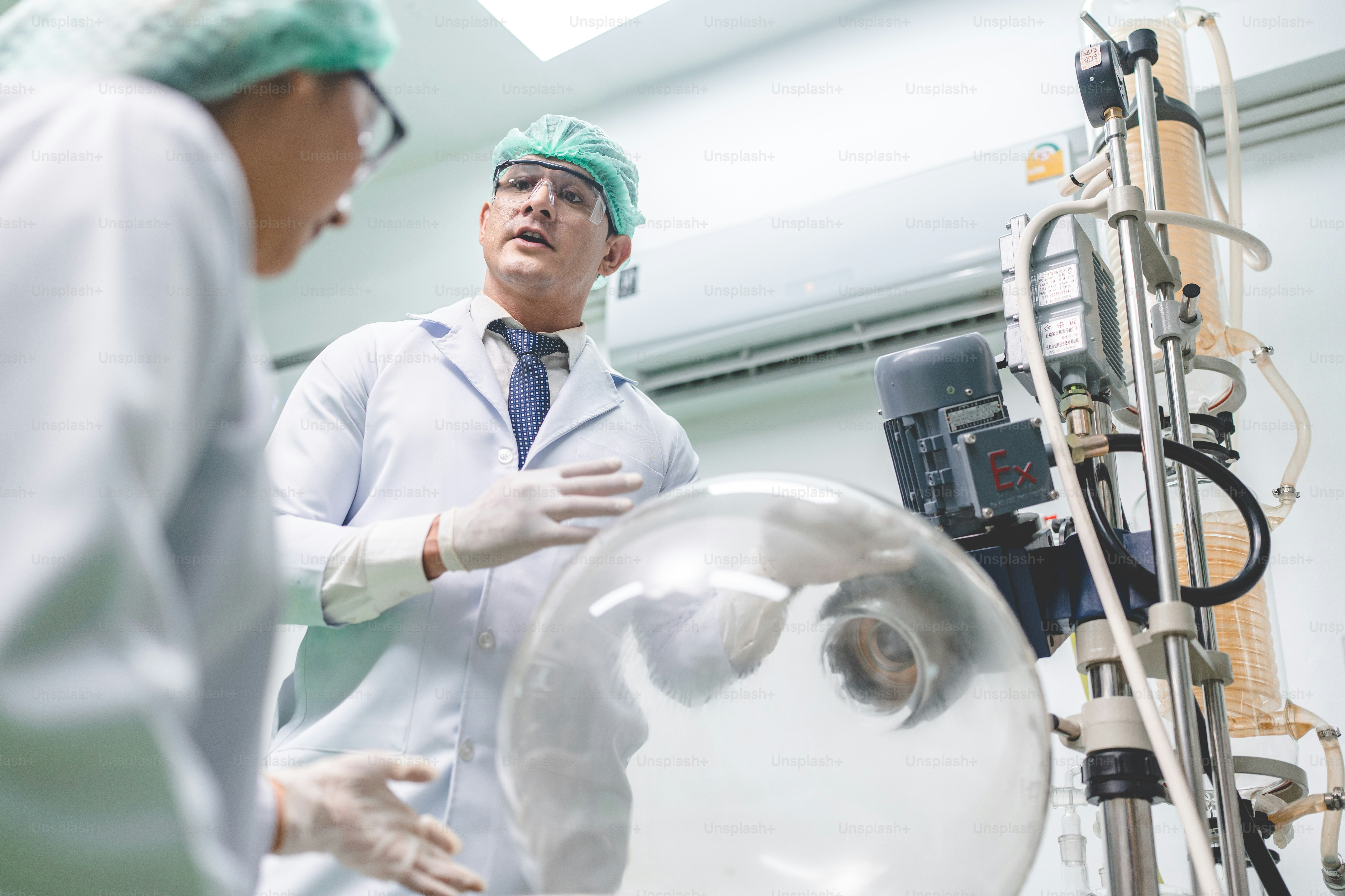 Zwei Wissenschaftler in Laborkitteln und Haarnetzen diskutieren über eine große Glas-Laborflasche