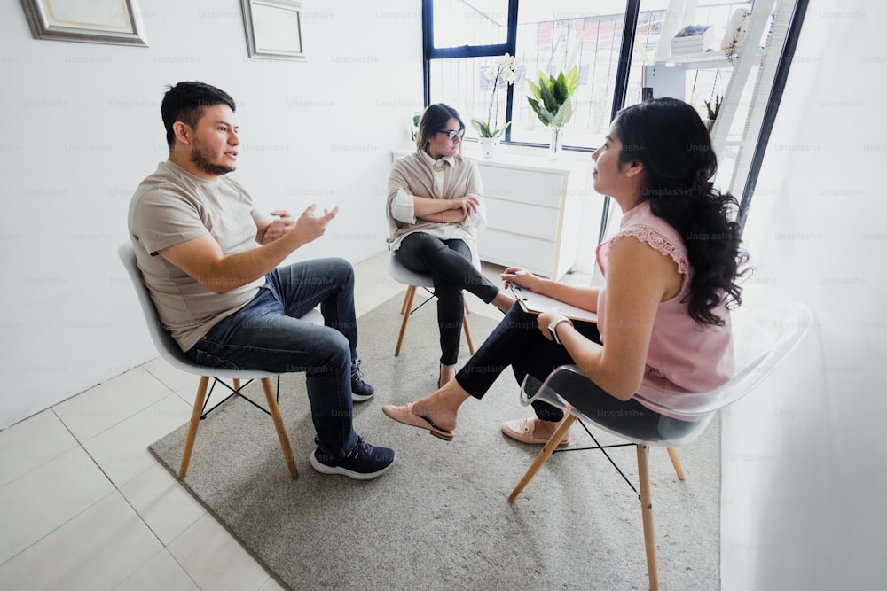 Hispanic young woman psychologist with couple patient in therapy talking about mental problems while doctor is listening and making notes in Mexico Latin America