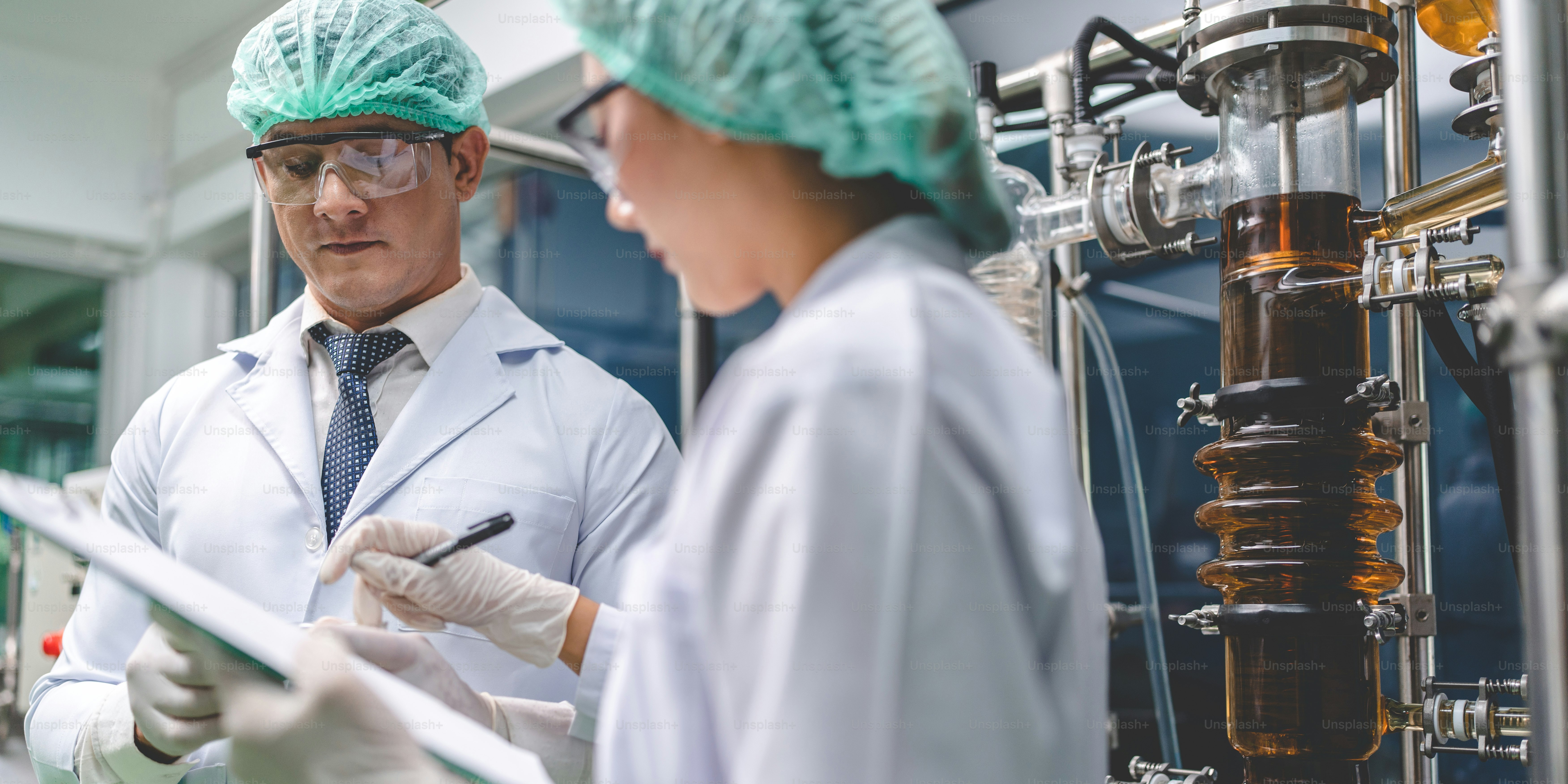 Zwei Wissenschaftler in Laborkitteln und Haarnetzen überprüfen Daten auf einem Klemmbrett