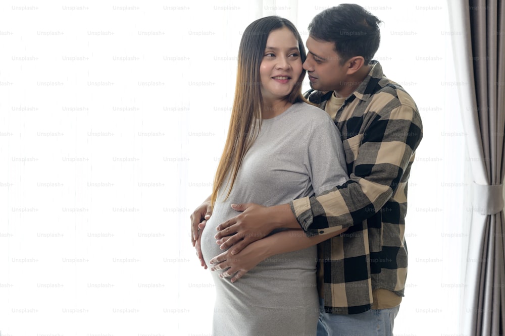 Giovane donna incinta con marito che abbraccia e aspetta un bambino a casa