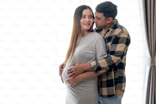 Young pregnant woman with husband embracing and expecting a baby at home