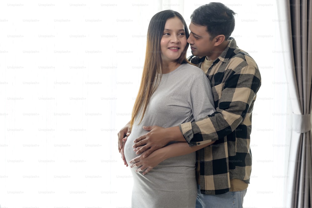 Young pregnant woman with husband embracing and expecting a baby at home