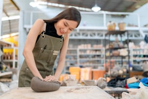 Gros plan de mains féminines travaillant sur un tour de potier, femme de sculpture féminine asiatique coloriant petit vase bol argile sur le tour de potier à l’atelier de studio à domicile