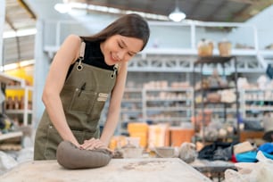 Close up of female hands working on potters wheel,asian female sculpture woman coloring small vase bowl clay on potter's wheel at home studio workshop