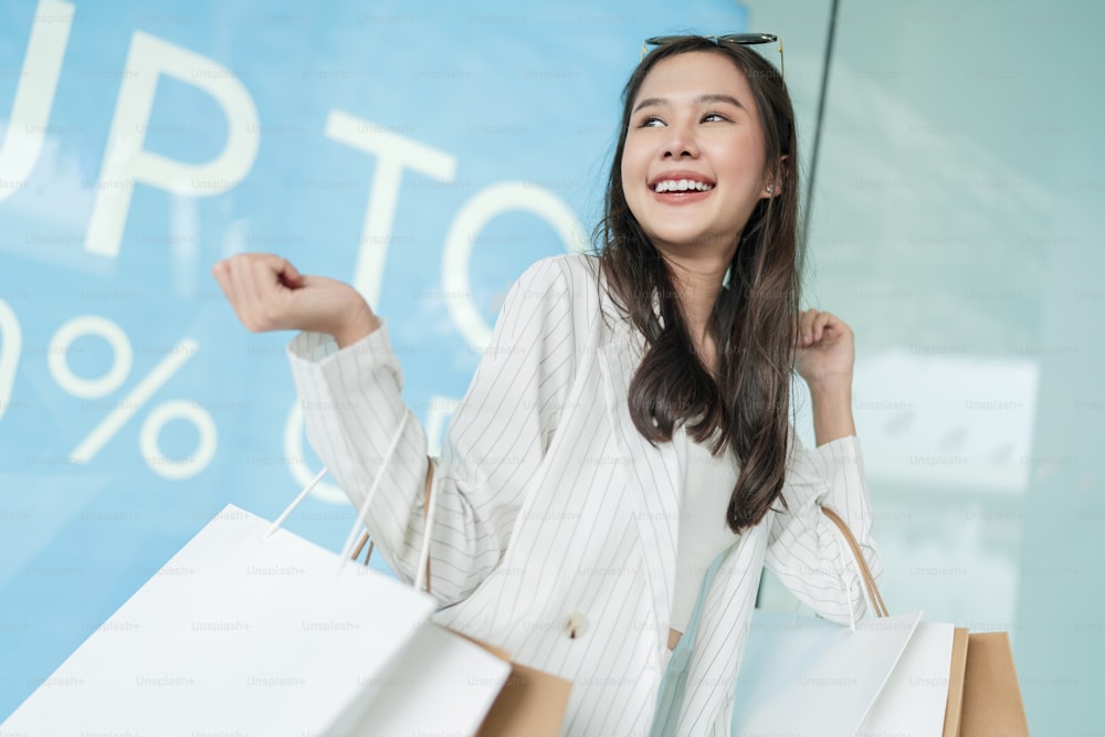 Filles de femme asiatique souriantes heureuses tenant un tas de sacs à provisions, femme rentrant chez elle après avoir fait du shopping, elle a acheté de nombreux vêtements à un prix raisonnable tout en vendant des prix réduits à la vitrine du magasin