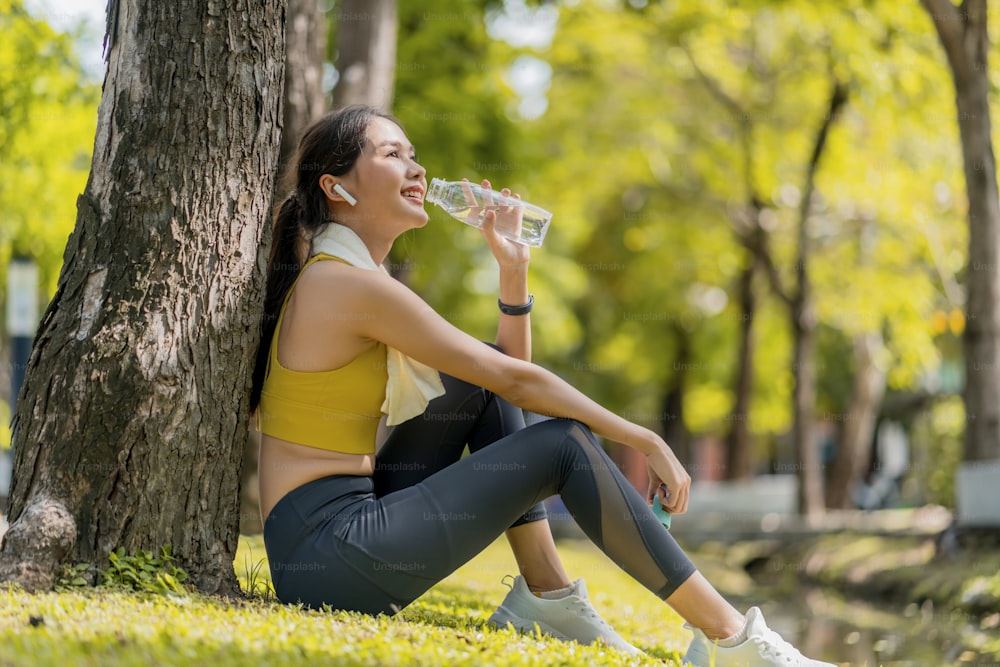 young Woman drinking water from bottle. asian female drinking water after exercises or sport. Beautiful fitness athlete woman wearing hat drinking water after work out exercising on sunset evening