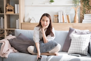 アジアの女性は自宅のリビングルームのソファでテレビを見ます