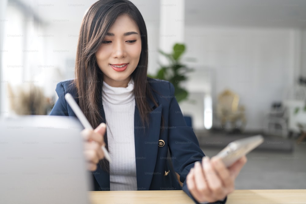 Smart Asian Business Frau Unternehmerin Kleinunternehmer formeller Anzug Tuch Arbeit Hand Eingabedaten Diagramm Informationen über Laptop Smartphone Tablet Arbeit von zu Hause aus