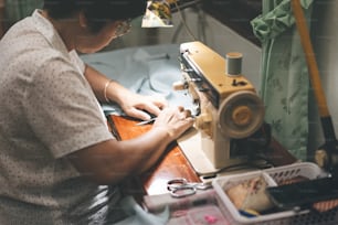 Sastre de recuperación de ancianos del sudeste asiático elaborando una tela con máquina de coser. Concepto maduro de trabajo en casa de la generación del baby boom. Momentos de la vida en retratos sinceros de personas auténticas.