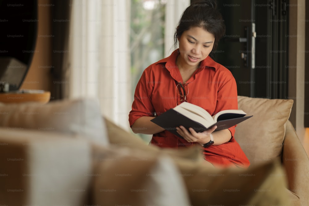casual relax at home,asian female adult woman cheerful smile peaceful expression reading book on sofa in living room at home morning moment happiness