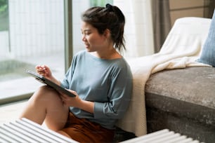 sitting on floor hand using tablet device for casual working from home,asian female woman cheerful hand writing on tablet sit on living room floor near sofa leisure weekend working in the house