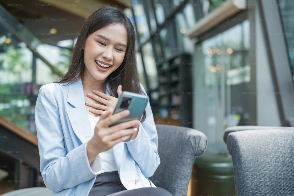 Schöne junge asiatische Frau benutzen Smartphone im Café erhalten E-Mail-Text gute Nachrichten KMU über ihren Kunden akzeptieren Vertrag handeln neues Projekt proporsal Junge Millennial Asien Frau gestikulieren Café