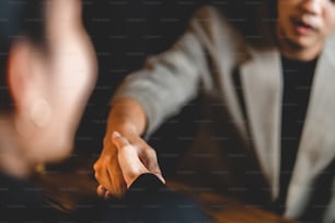 Closeup of hands of two young and successful male business people shaking hands over wooden table with laptop and digital tablet while sealing deal of partnership