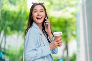 Asiatique femelle décontracté se détendre nomade numérique freelance expatrié programmateur intelligent décontracté tissu marcher sur le trottoir urbain ville avec tenir smartphone souriant de bonne humeur positif sentiment rétrogradant mode de vie